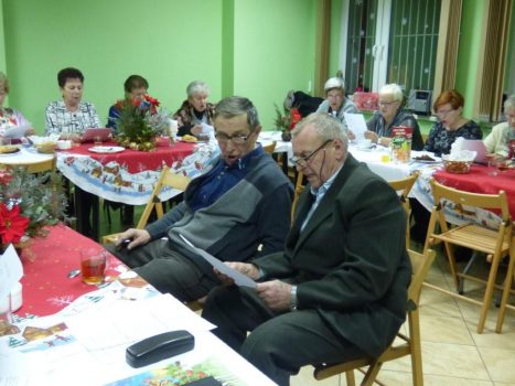 Seniorzy siedzą przy stole w czasie Spotkania Opłatkowo-Karnawałowego i śpiewają kolędy