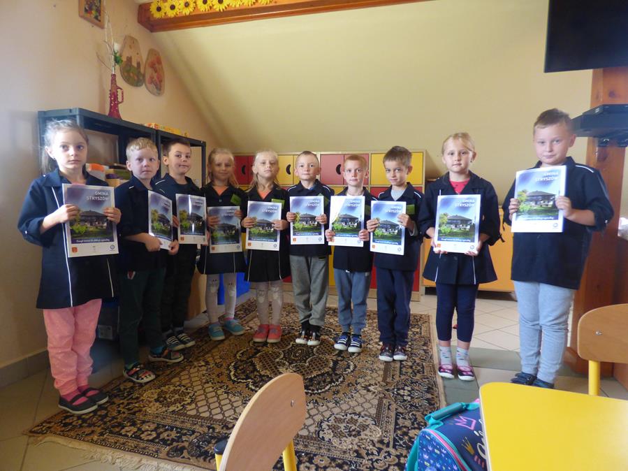 Dzieci z Dąbrówki stoją w półokręgu trzymając w rękach zeszyty ćwiczeń pozują do zdjęcia.