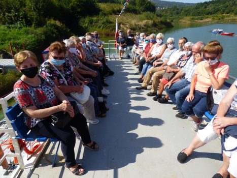 Seniorzy siedzą na ławeczkach na górnym pokładzie statku płynącego po Jeziorze Mucharskim.