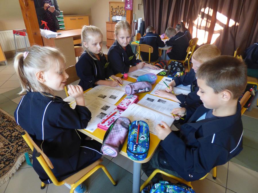 Dzieci z Dąbrówki siedzą przy stolikach, przed nimi leżą otwarte zeszyty ćwiczeń do lekcji regionalizmu.