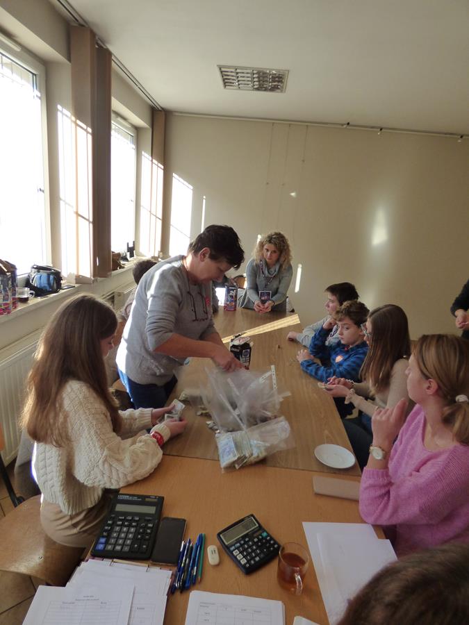 wolontariusze z Łękawicy wraz z Pracownikiem Biblioteki siedzą przy stole, liczą pieniądze i wkładają je do woreczków