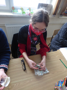 Wolontariuszka Zofia siedzi przy stole i liczy pieniądze.