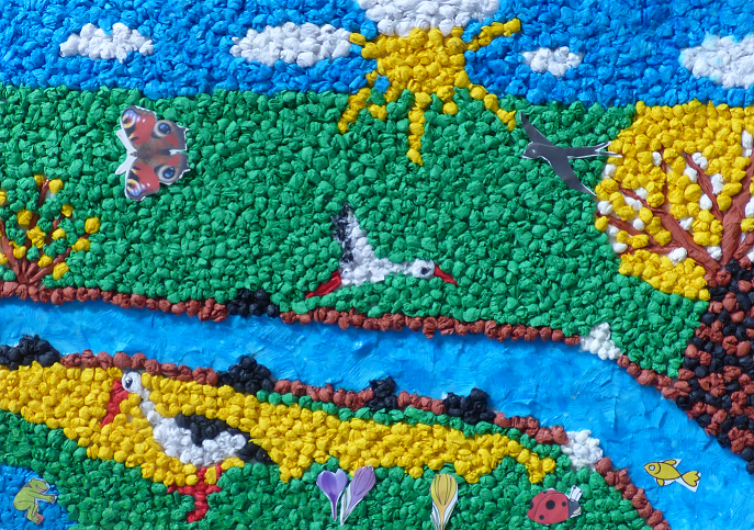 zdjęcie przedstawia pracę plastyczną uczestnika konkursu z klasy 1, na której widać wiosenny zielony krajobraz, w dole płynie rzeczka, na niebie latają bociany, motyle i jaskółki, drzewa kwitną na żółto, na niebie świeci słońce.