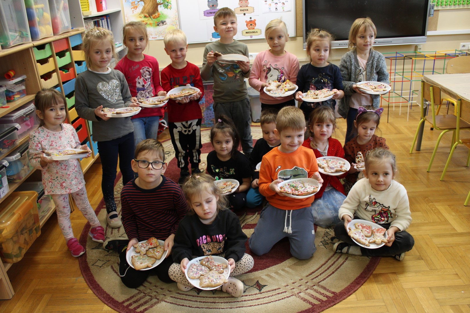 Przedszkolaki z Łękawicy stoją i siedzą ustawieni do zdjęcia grupowego, trzymają w rękach talerzyki z udekorowanymi pierniczkami.