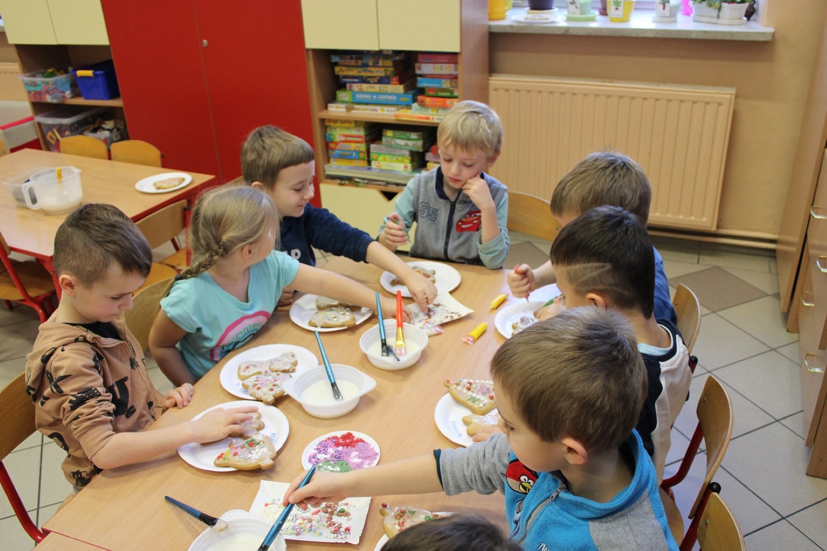 Siedmioro przedszkolaków ze Stryszowa siedzi wokół stołu i dekoruje pierniczki.