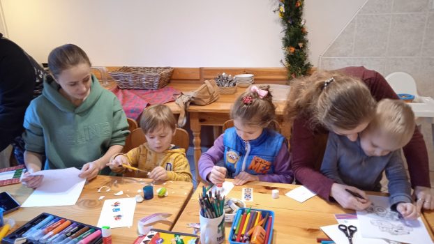 Dwie mamy i trójka dzieci siedzą przy stole i wycinają elementy potrzebne do wykonania ramki na zdjęcia.