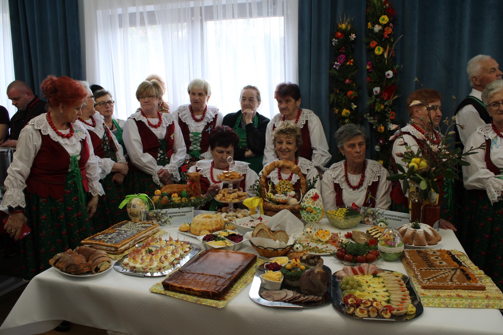 Grupa kobiet przebranan w tradycyjne stroje przed nimi stół z wilkanocnymi spejałami.