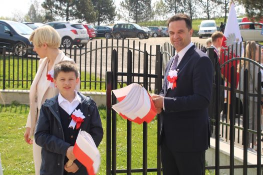 Pan wójt Gminy Stryszów Szymon Duman, jego żona i syn stoją w bramie prowadzącej do kościoła i trzymają w rękach biało-czerwone chorągiewki.