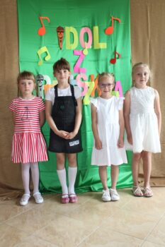 cztery dziewczynki z klasy "0" stoją na tle zielonej dekoracji i pozują do zdjęcia po występach konkursowych