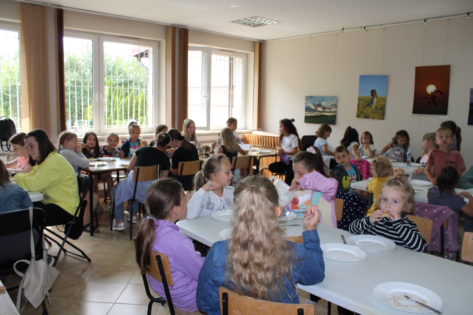 Zdjęcie przedstawia grupę trzydziestu jeden dzieci, które robią naleśniki na świetlicy GOK podczas wakacyjnych zajęć kulinarnych Klubu „Zosi Samosi”.
