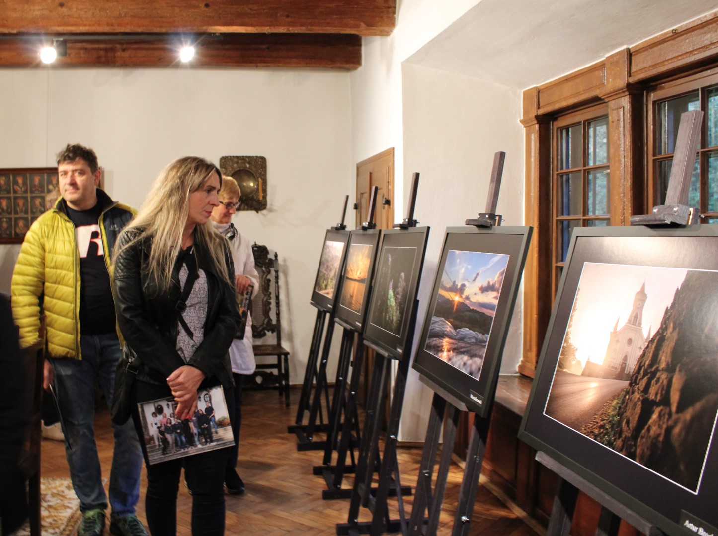 W jednym z pomieszczeń Dworu w Stryszowie stoją ustawione na sztalugach zdjęcia projektowe, trzy osoby przechodzą oglądając je.